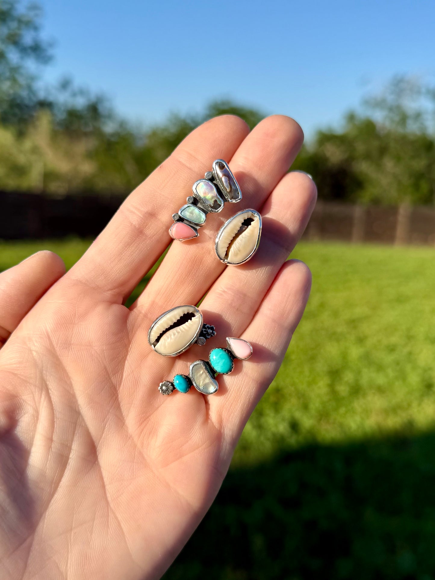 Cowrie and abalone shell rings being shown together showing iridescent rainbow tones