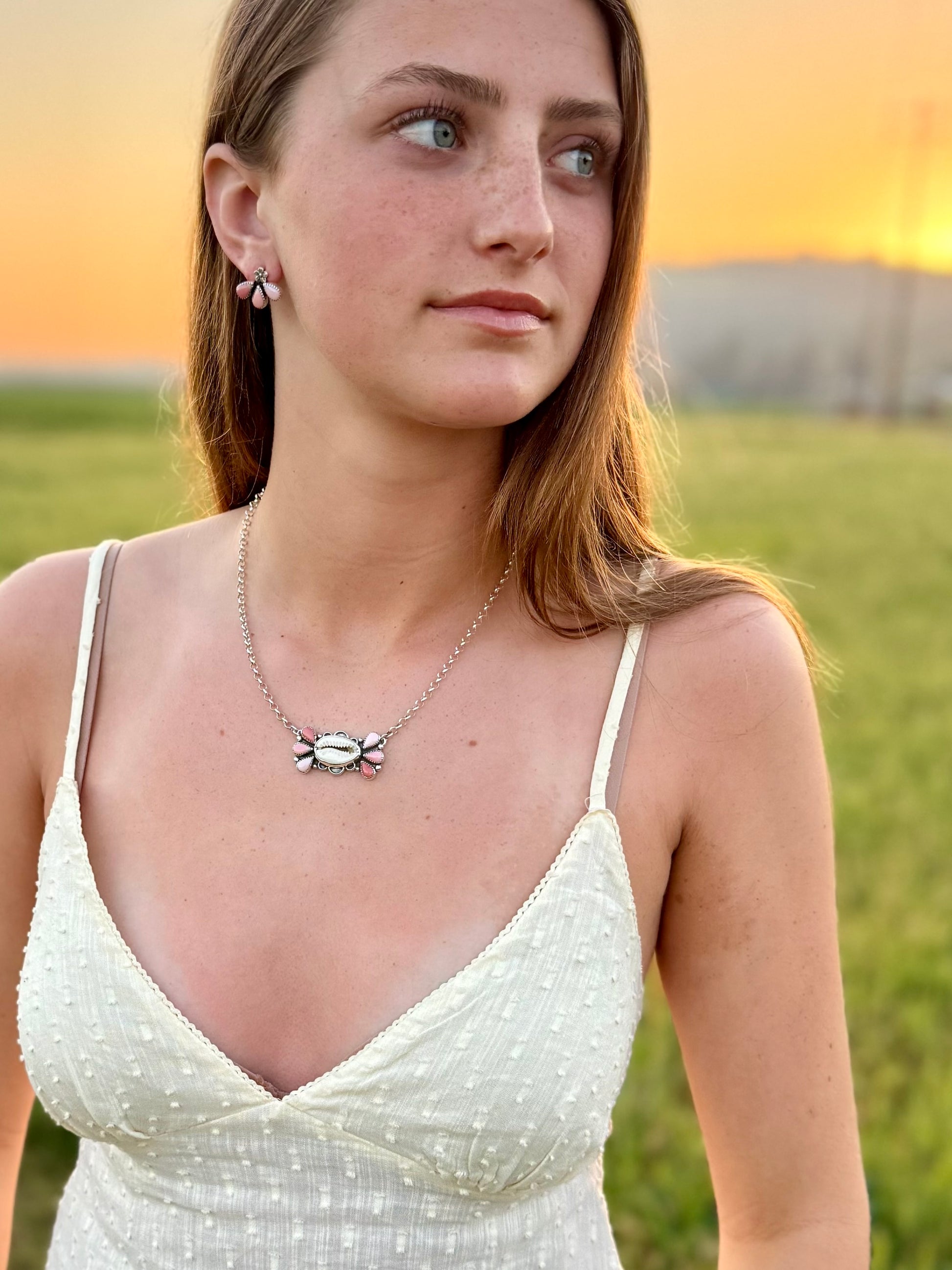 Woman wearing a necklace with a butterfly pendant in a field at sunset