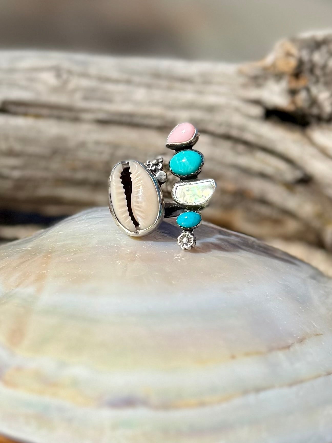 Silver ring with colorful  beach stones shells and turquoise on a shell with driftwood in the background