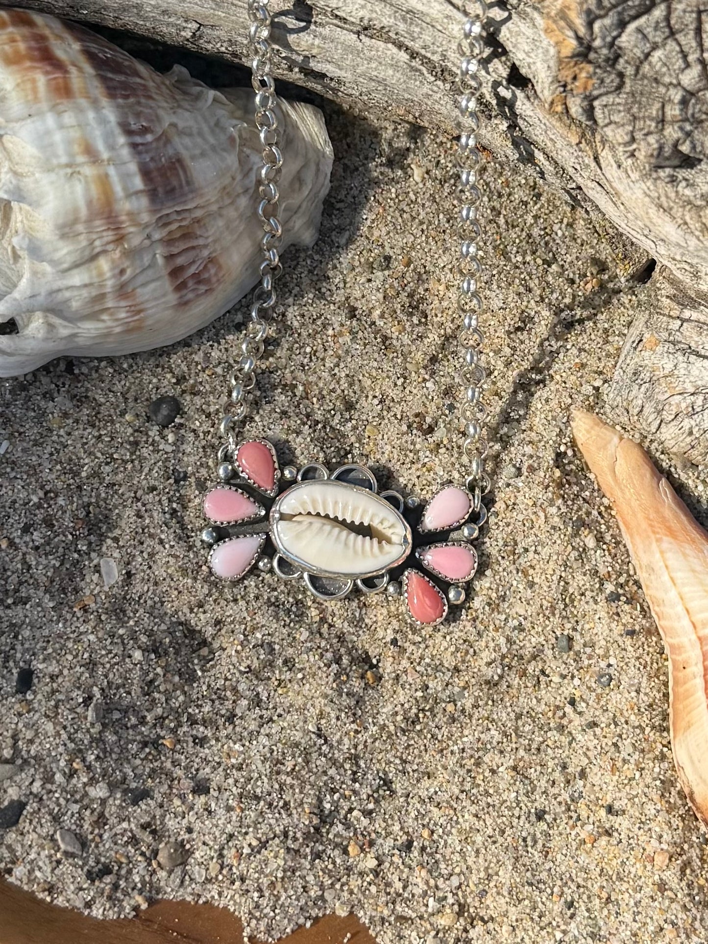 Necklace with a cowrie shell pendant on sand and shells