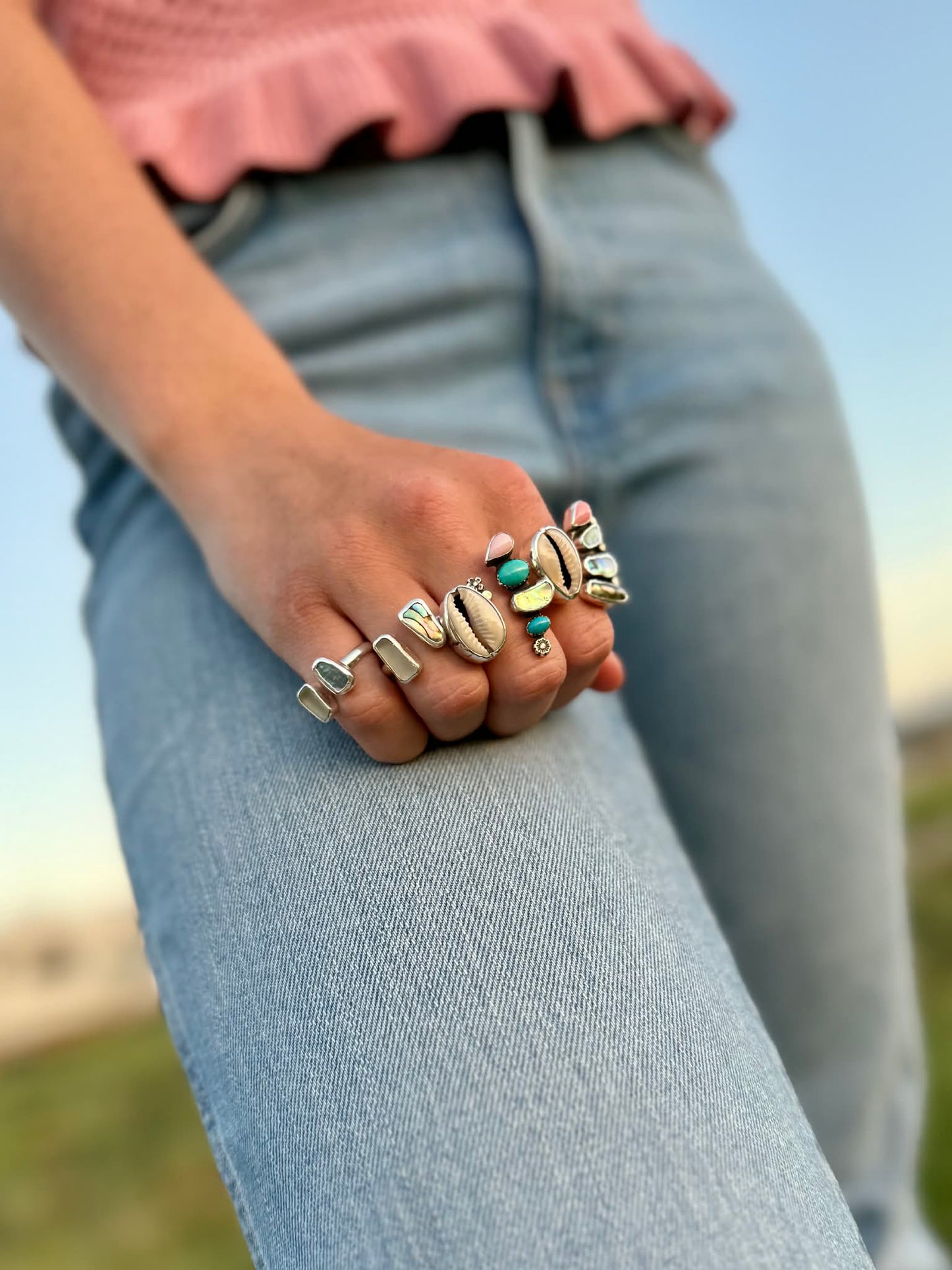 Close-up of a person's hand wearing multiple rings with a blurred natural background