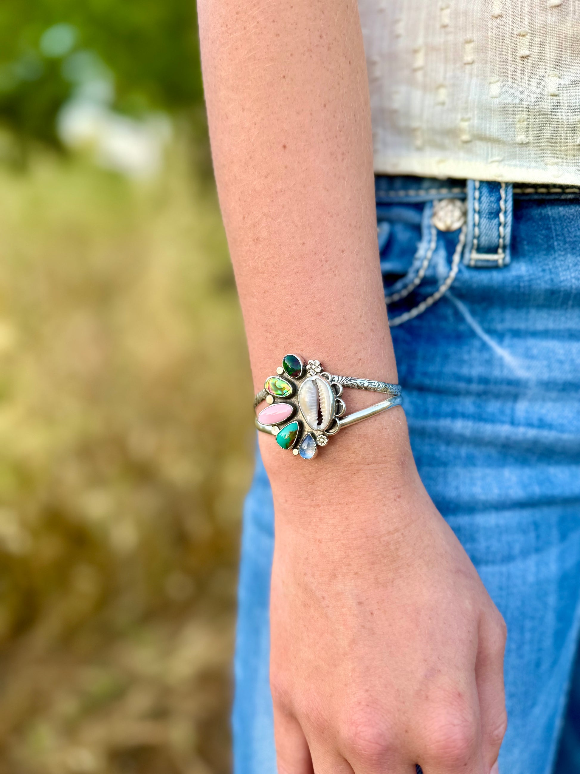 Close-up of a person's wrist wearing a silver bracelet with colorful stones against a blurred natural background.