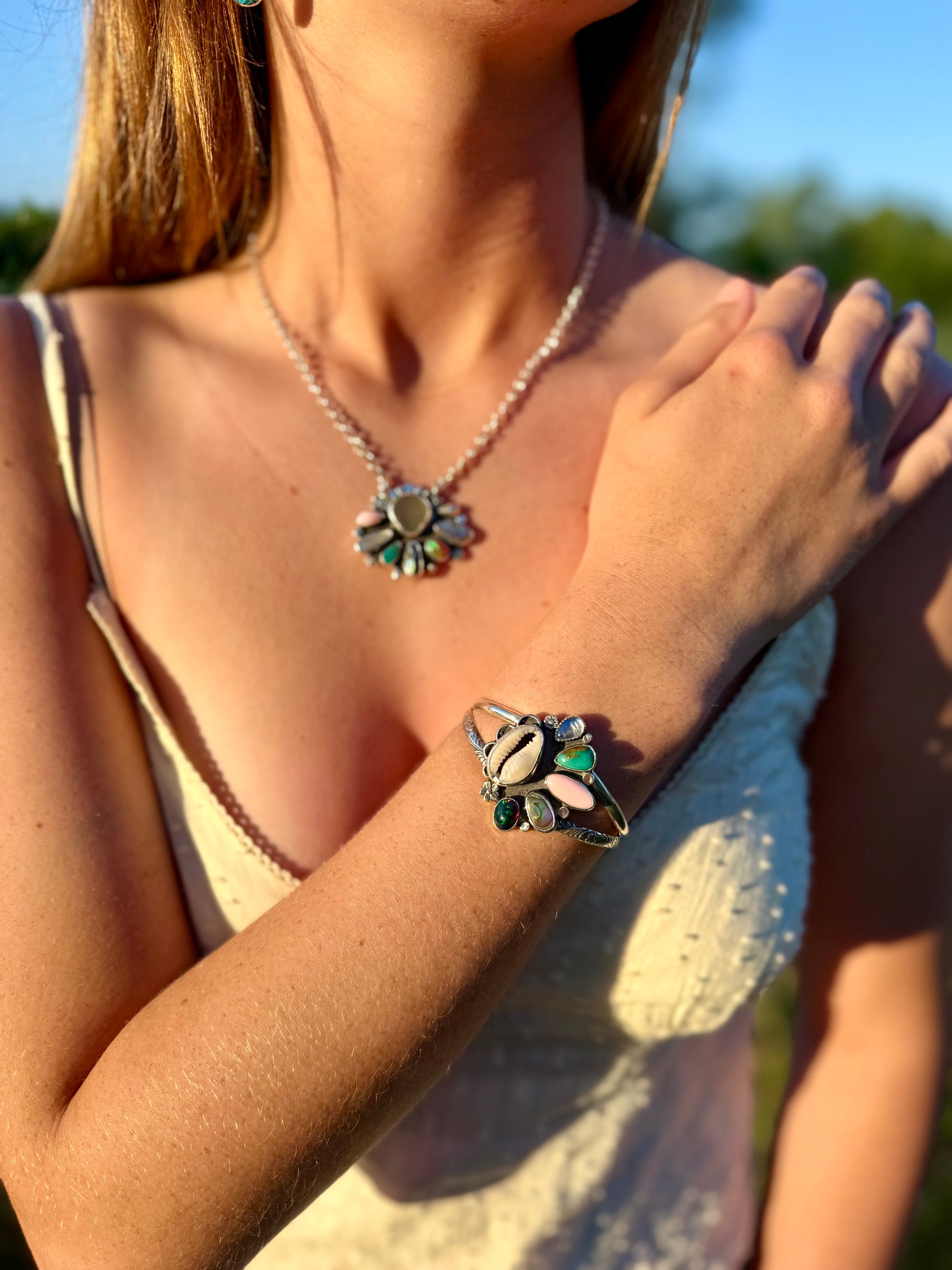 Close-up of a person wearing a coastal inspired necklace and bracelet with gemstones outdoors.