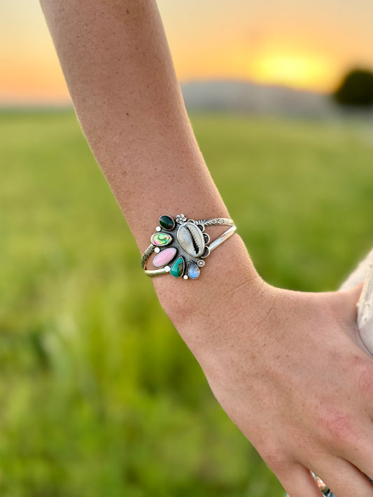 colorful multi stone bracelet cuff showing the cowrie shell abalone opal moonstone and conch with sunset background