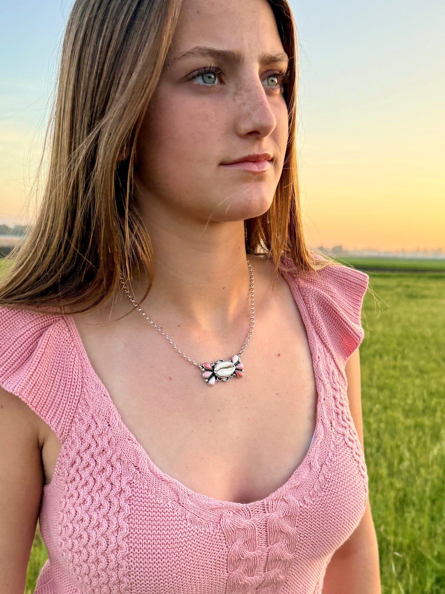 Woman wearing a Cowrie shell and pink conch ombre necklace in a field at sunset