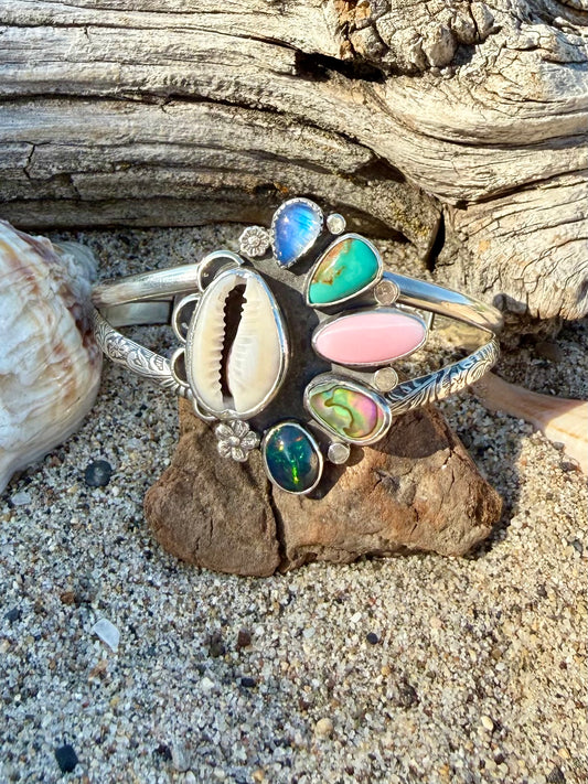 Silver bracelet with colorful stones on a drift wood and sandy surface