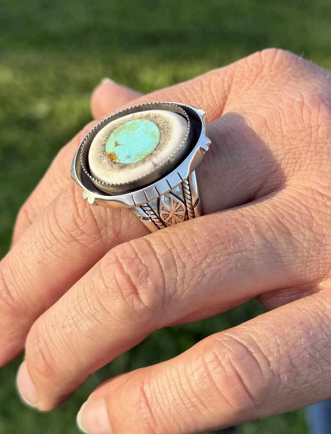 Hand wearing a silver ring with a turquoise stone against a grassy background
