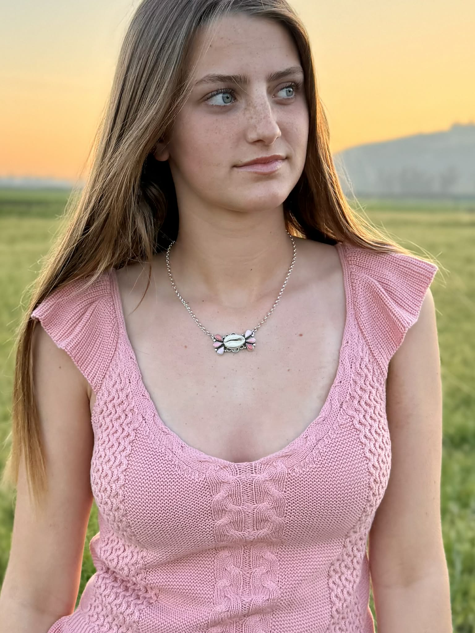 Woman wearing a cowrie shell with ombre pink conch necklace in a field at sunset