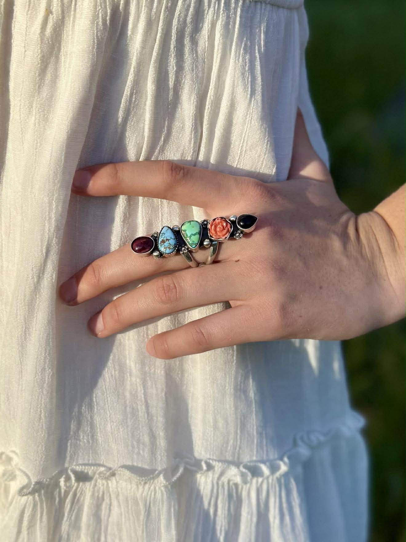 Hand wearing a colorful ring with gemstones against a white dress.