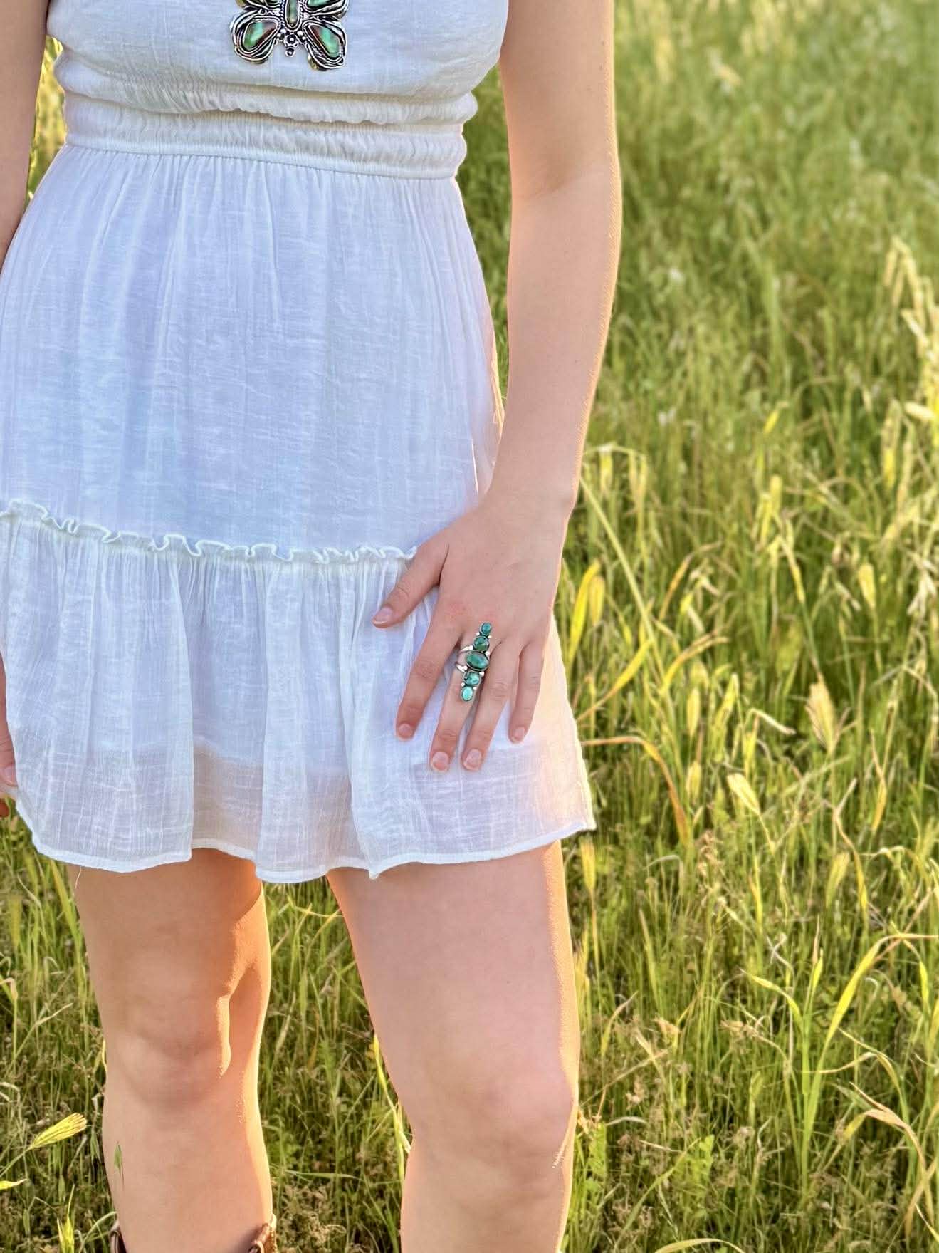 Person wearing a white dress with an ombre Royston crawler ring in a grassy field