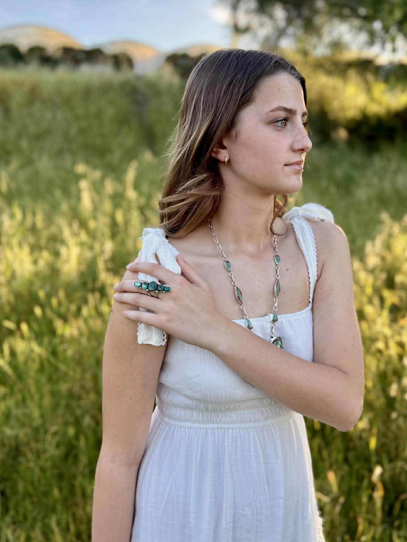 Woman in a white dress standing in a grassy field showing ombre turquoise ring