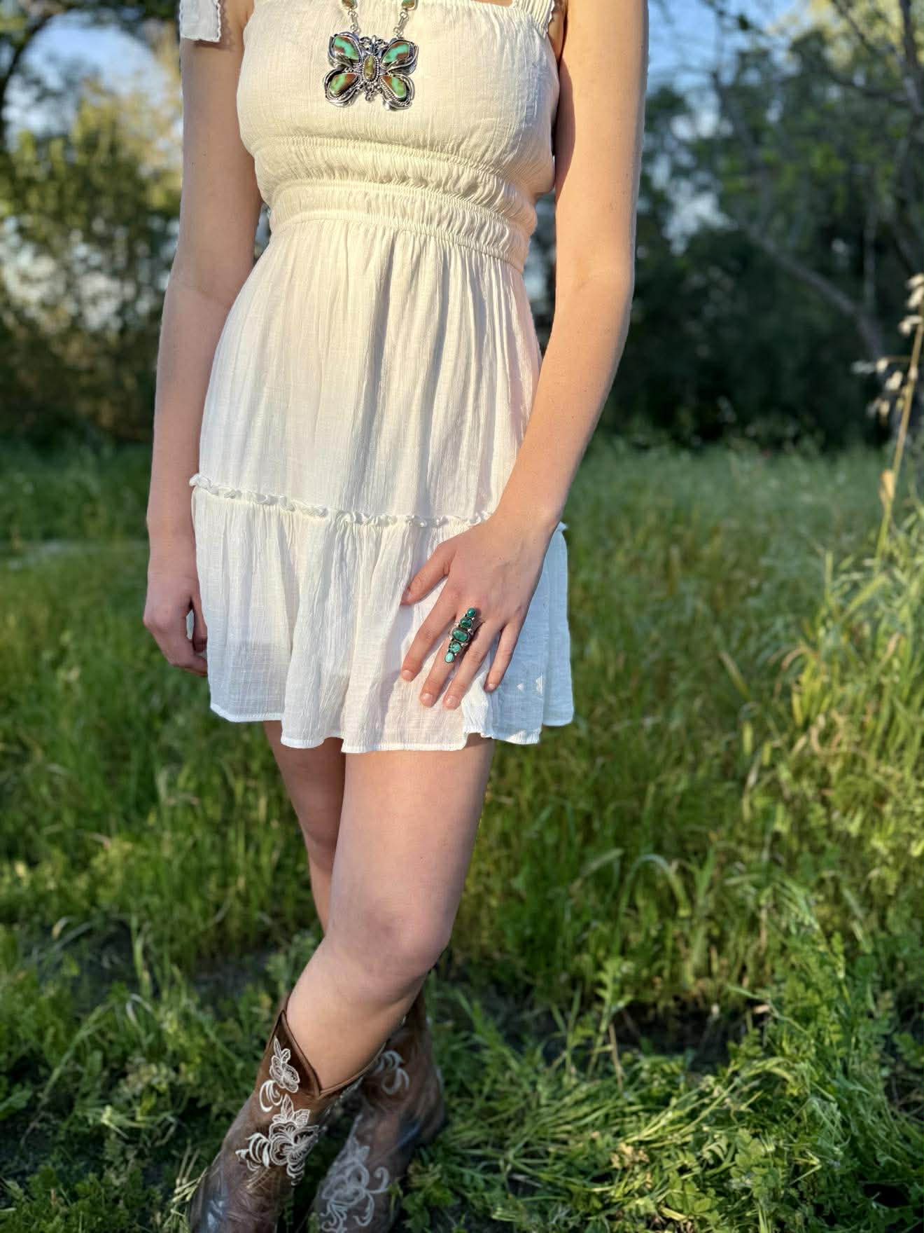 Person wearing a white dress with a butterfly accessory in a grassy outdoor setting