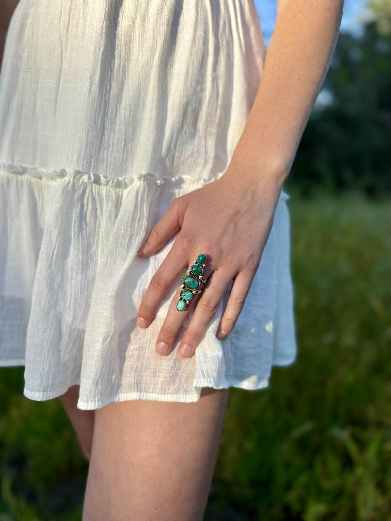 Person wearing a white dress with a green ring in a natural setting