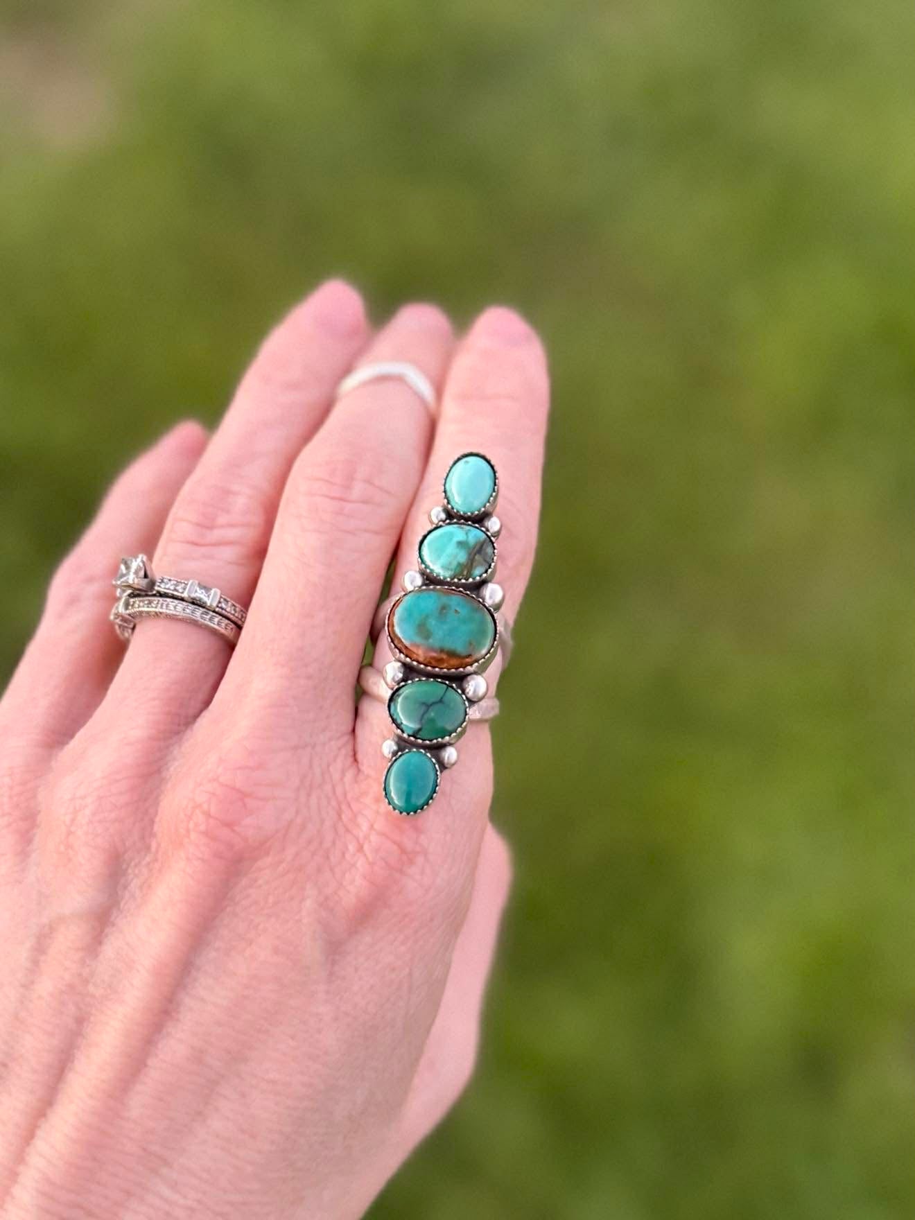 Hand wearing a turquoise stone ring with a blurred green background