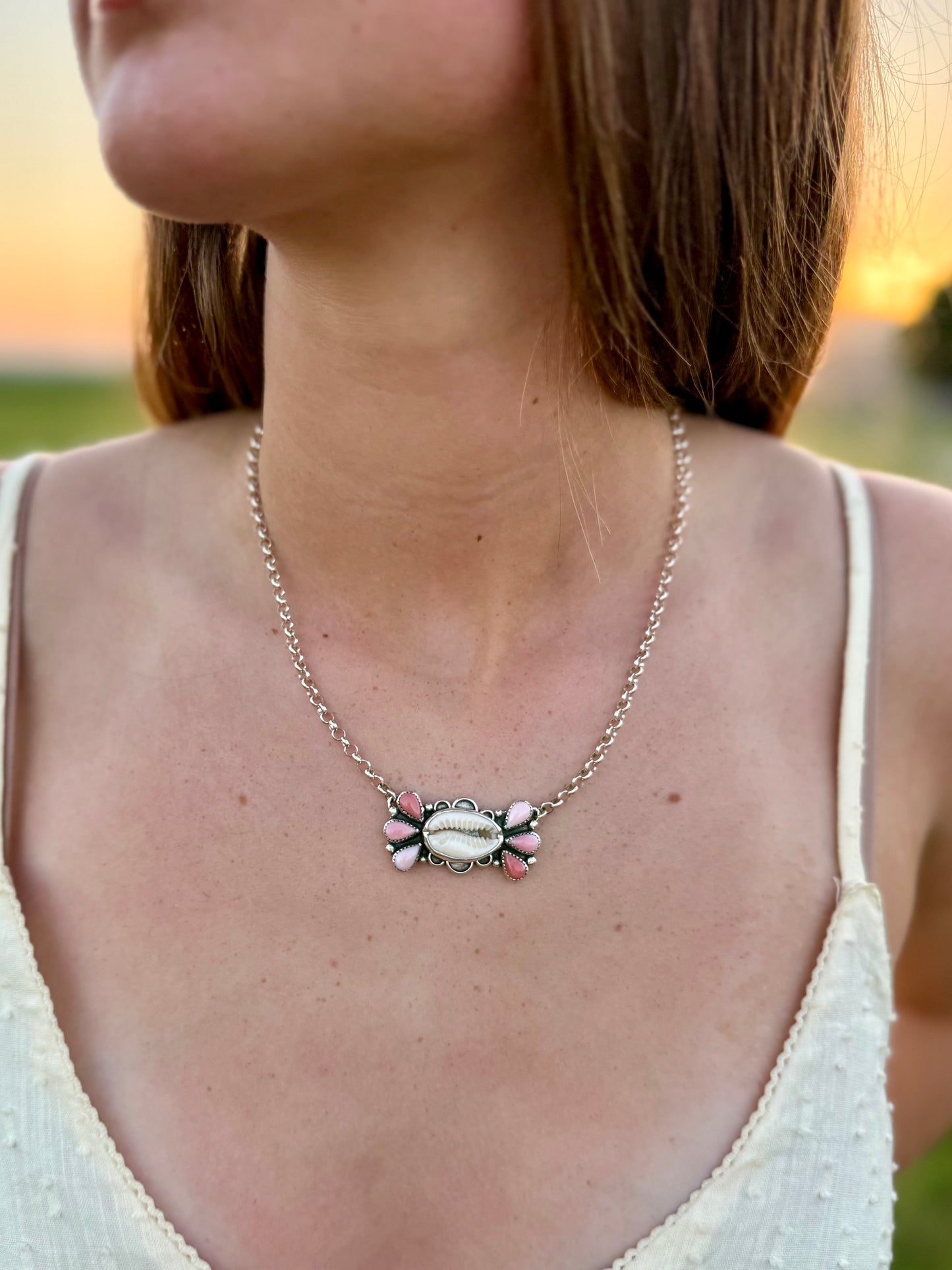 Person wearing a cowrie shell and ombre pink conch necklace handmade with sterling silver
