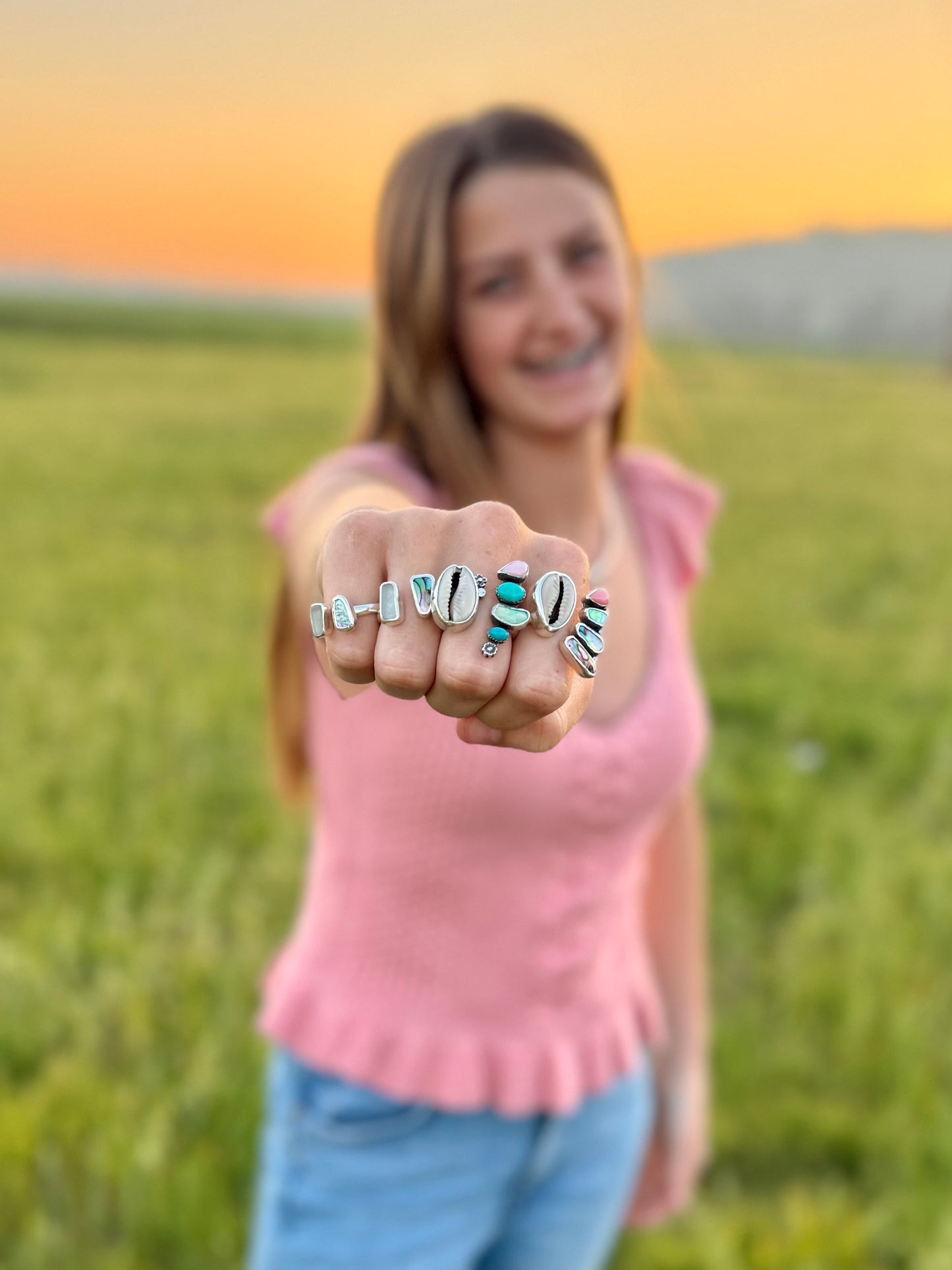 women showing 4 rings together on her hand with beach stones and shells