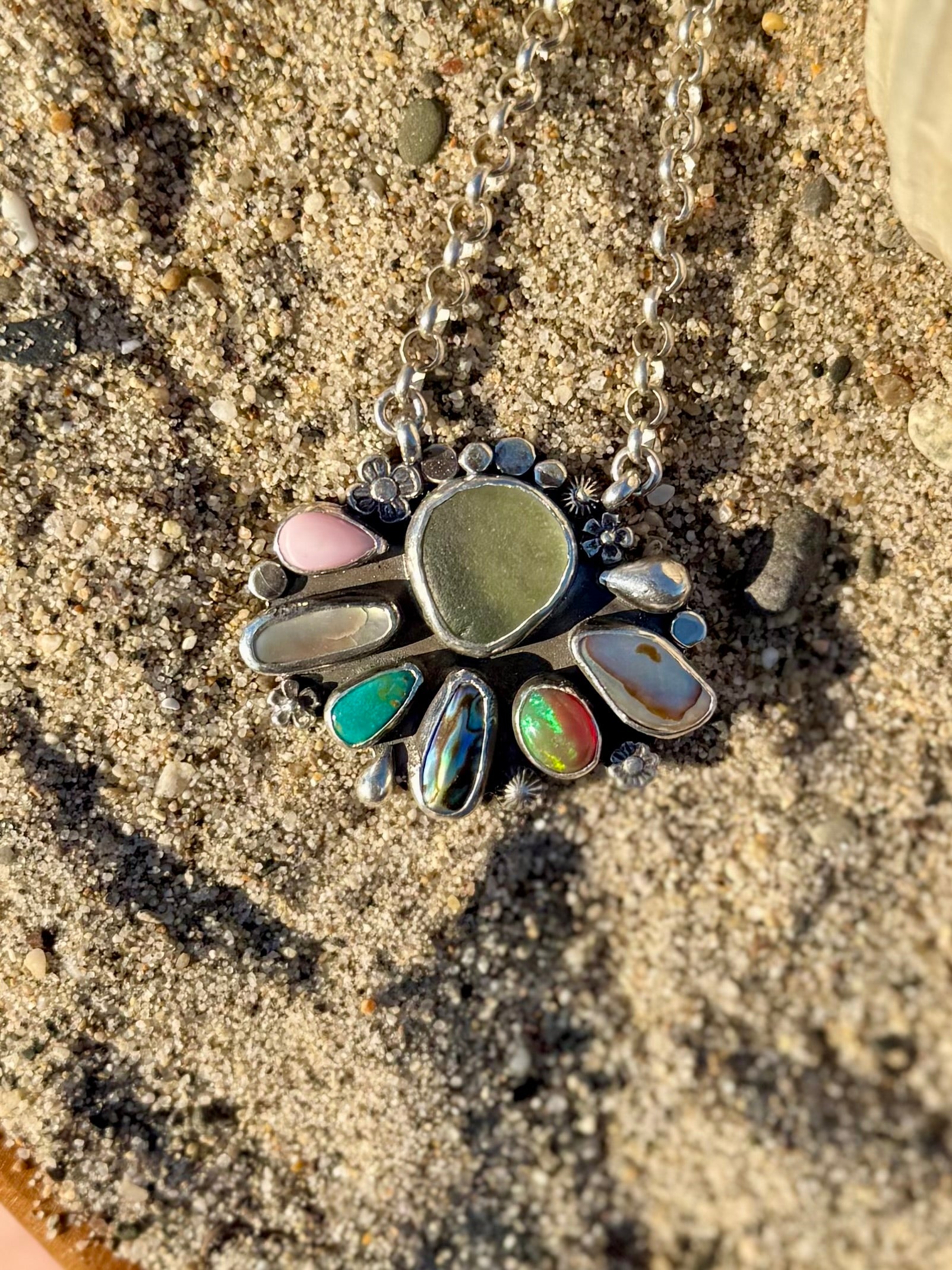 Necklace with a pendant featuring colorful stones on a sandy coastal background