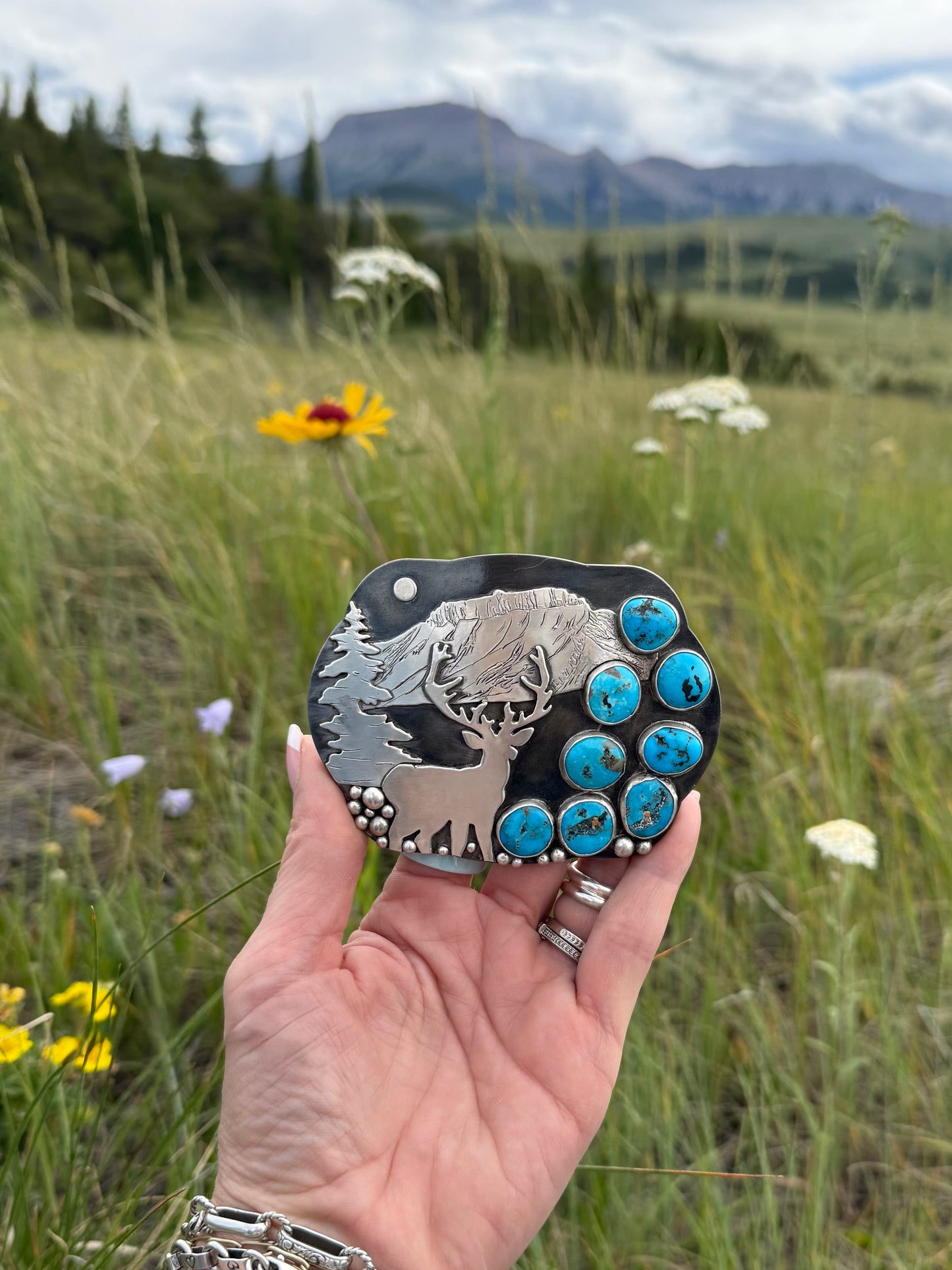 Hand engraved Ithaca Peak Turquoise elk belt buckle with sterling silver Ear Mountain and pine tree scene by Donnalee Silver.