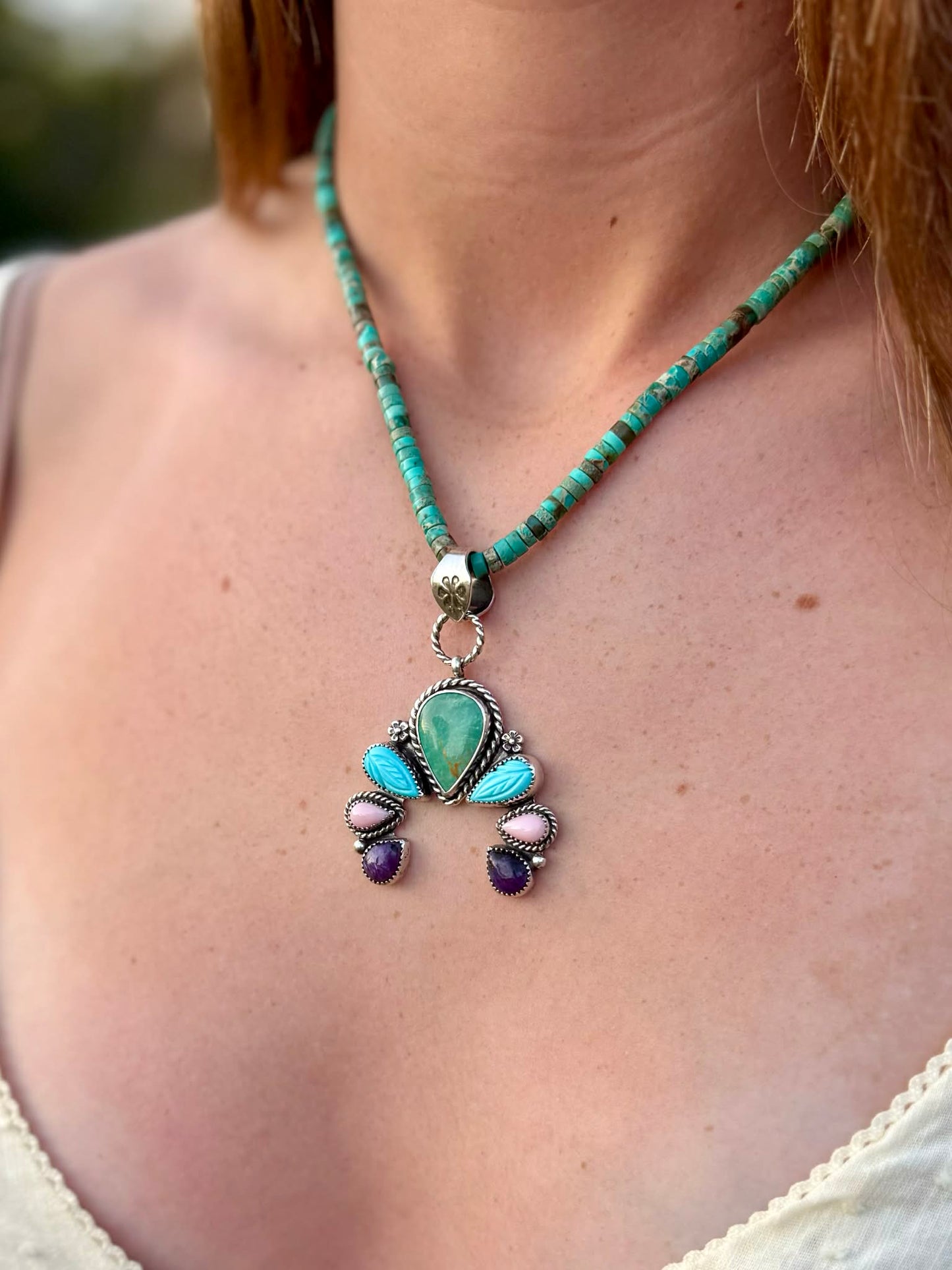 Necklace with a pendant featuring turquoise and other stones on a person's neck.