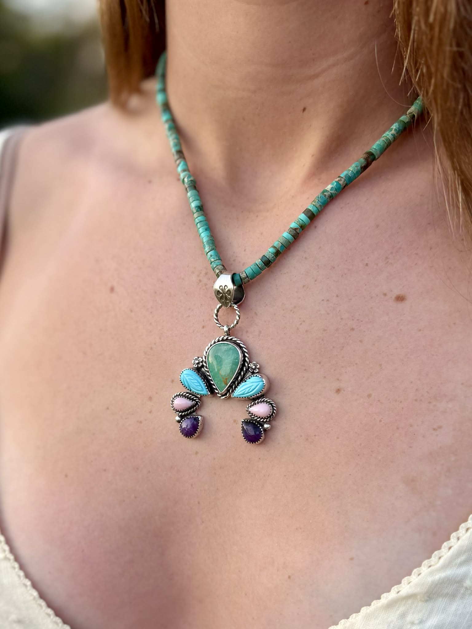 Necklace with a pendant featuring turquoise and other stones on a person's neck.