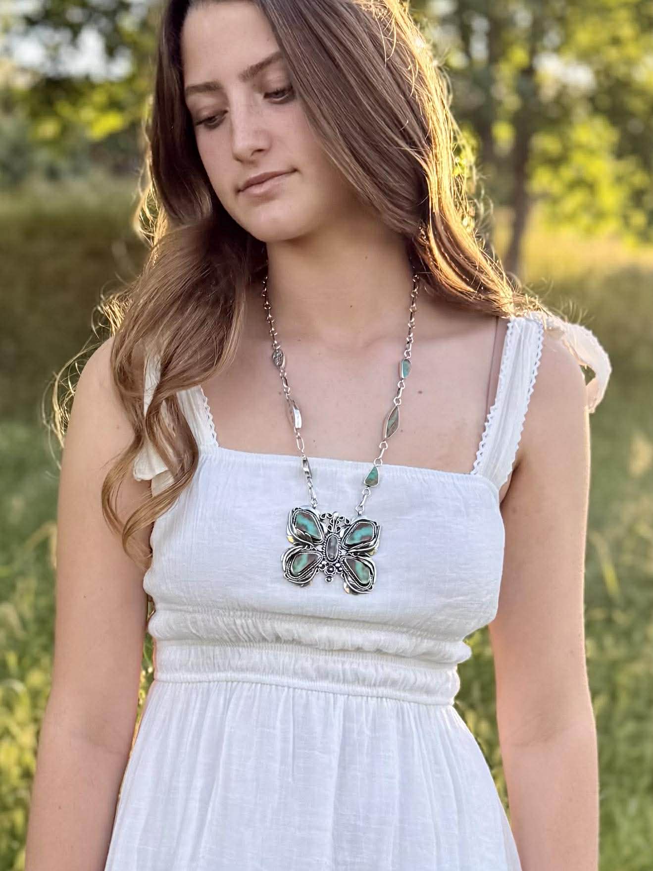 Woman wearing a white dress with a butterfly necklace in a natural setting