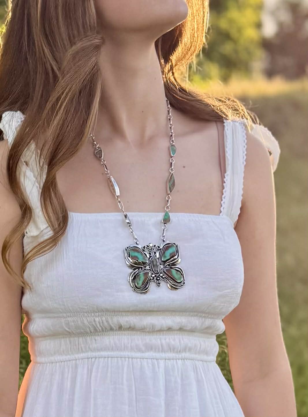 Butterfly necklace worn by a person in a white dress outdoors