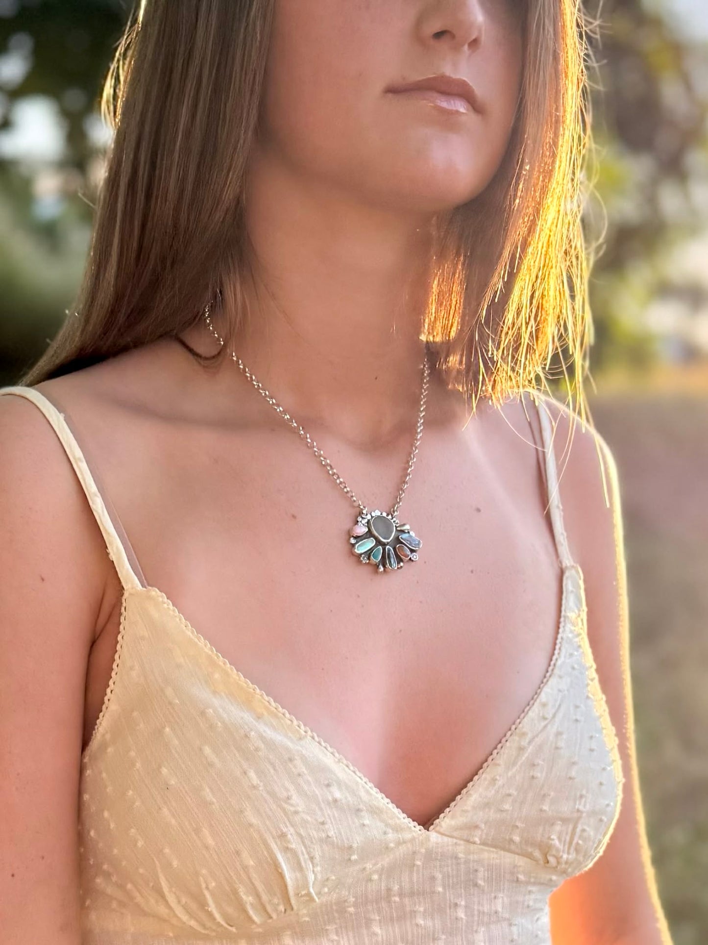 Woman wearing a delicate necklace with a floral pendant in a natural setting
