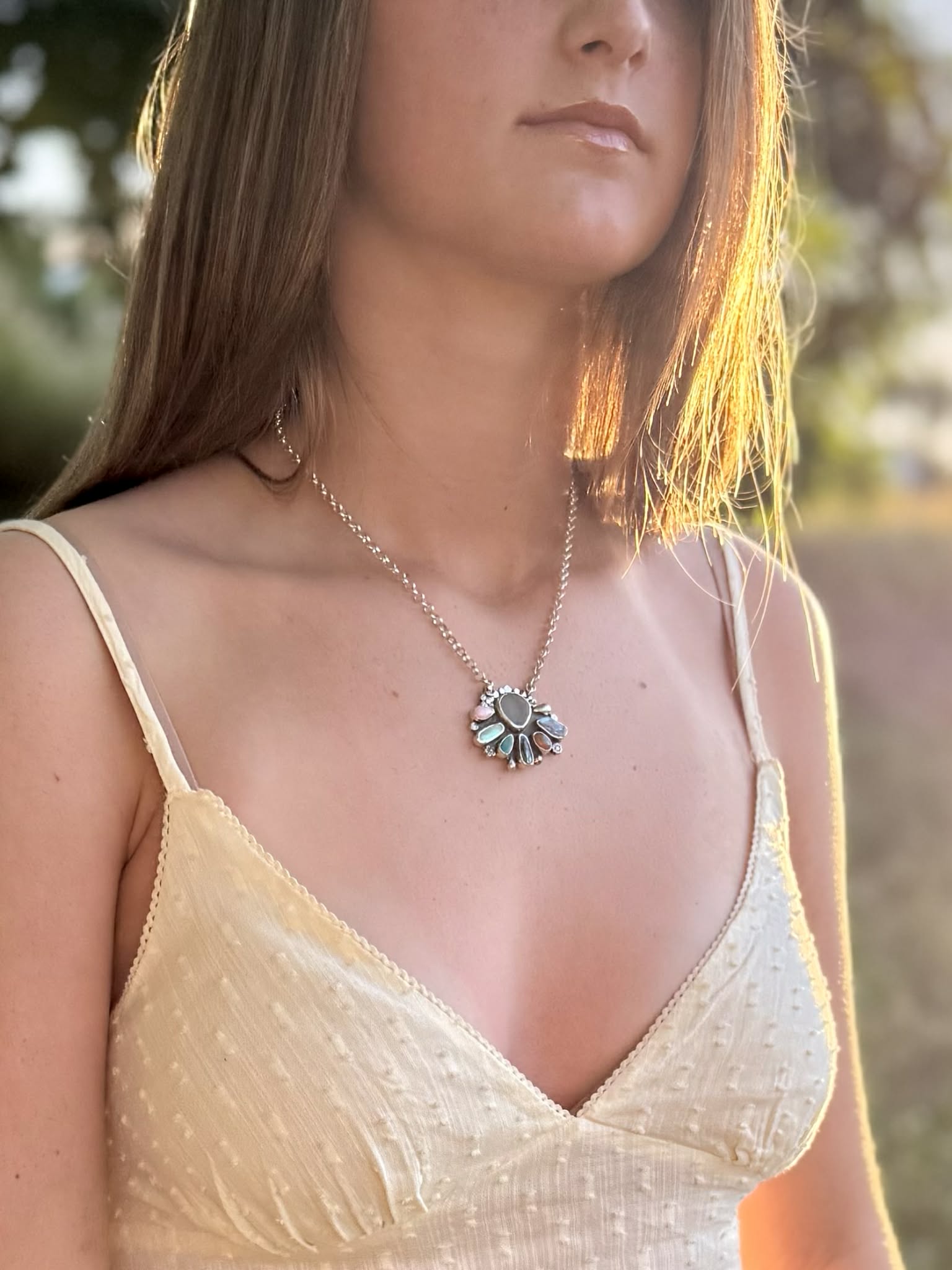 Woman wearing a delicate necklace with a floral pendant in a natural setting